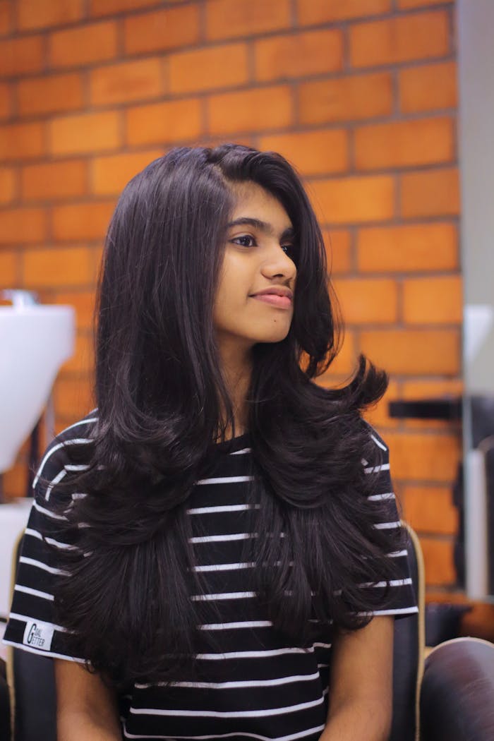 Portrait of a young woman with long, flowing hair in an indoor setting with brick background.
